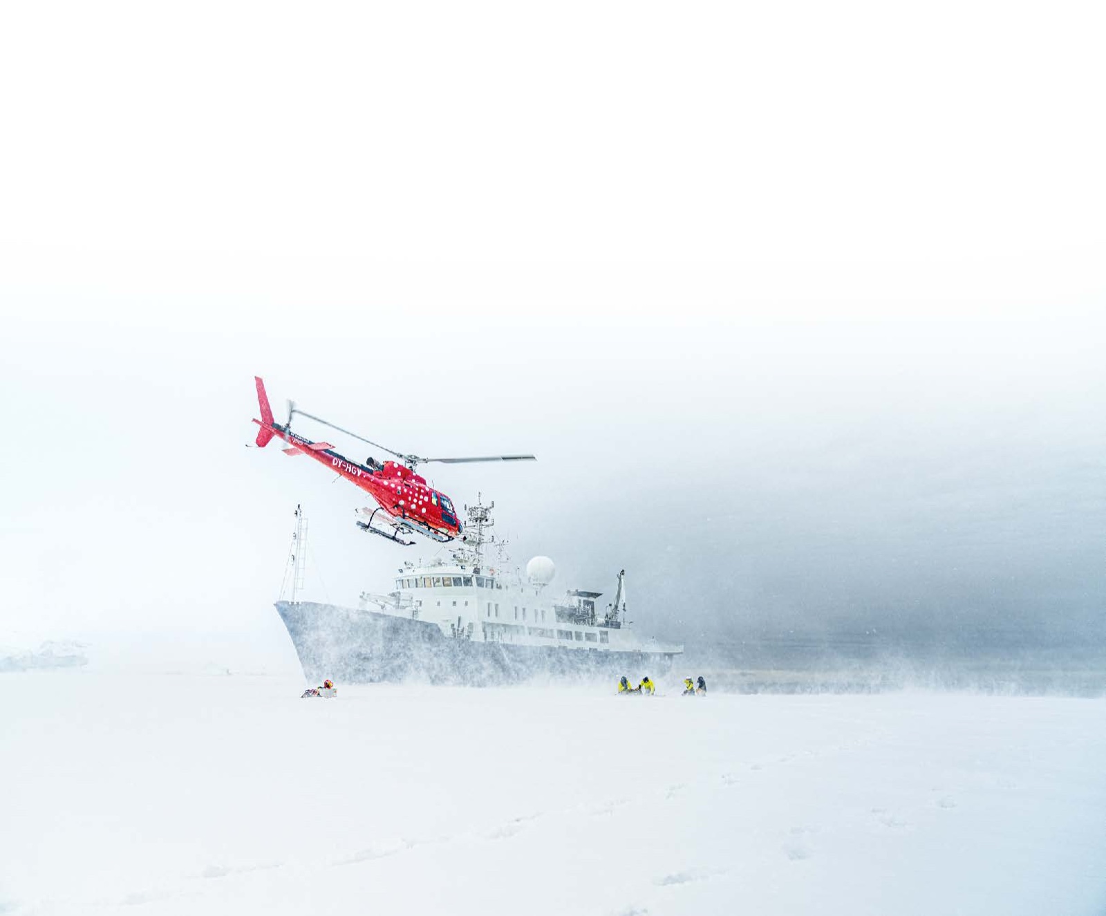 Helicopter lifting off an expedition yacht in a snowstorm